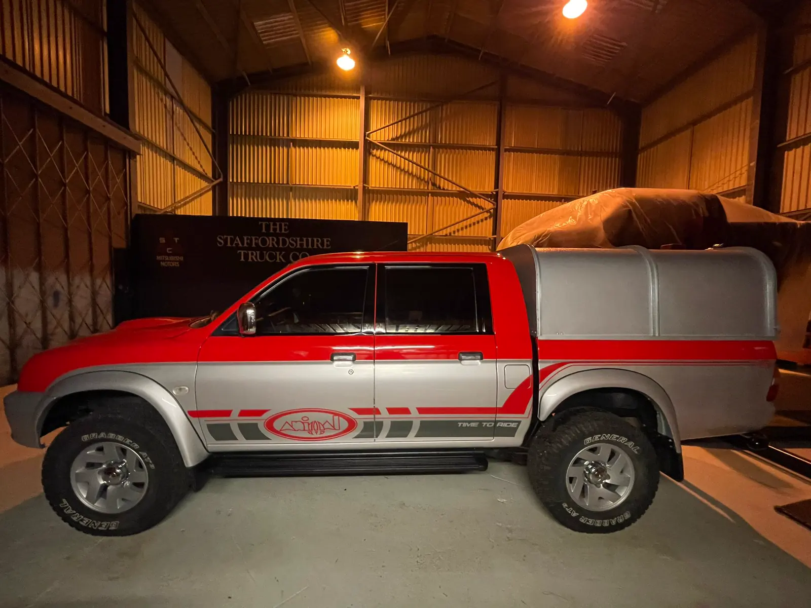 A refurbished red and silver Mitsubishi L200 K74 with its canopy fitted, inside the STC workshop