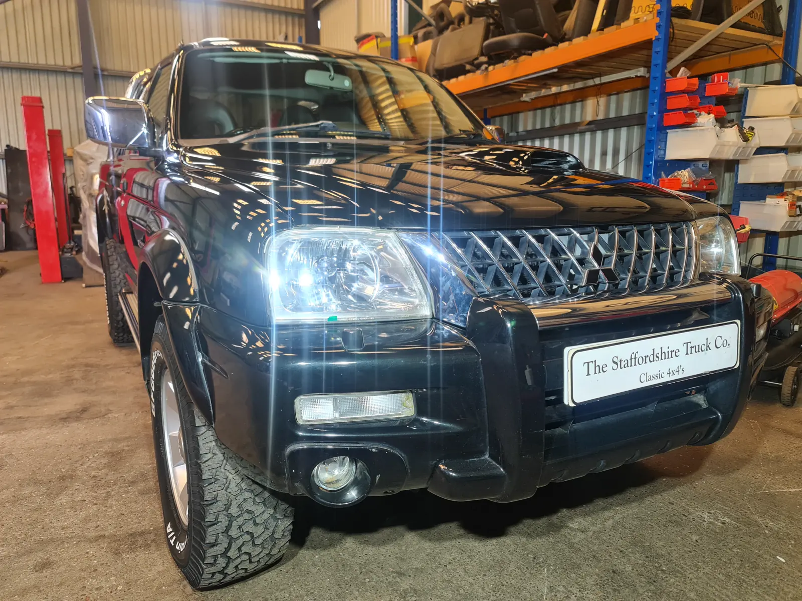 A black Mitsubishi L200 K74 on the ramp under the workshop lights