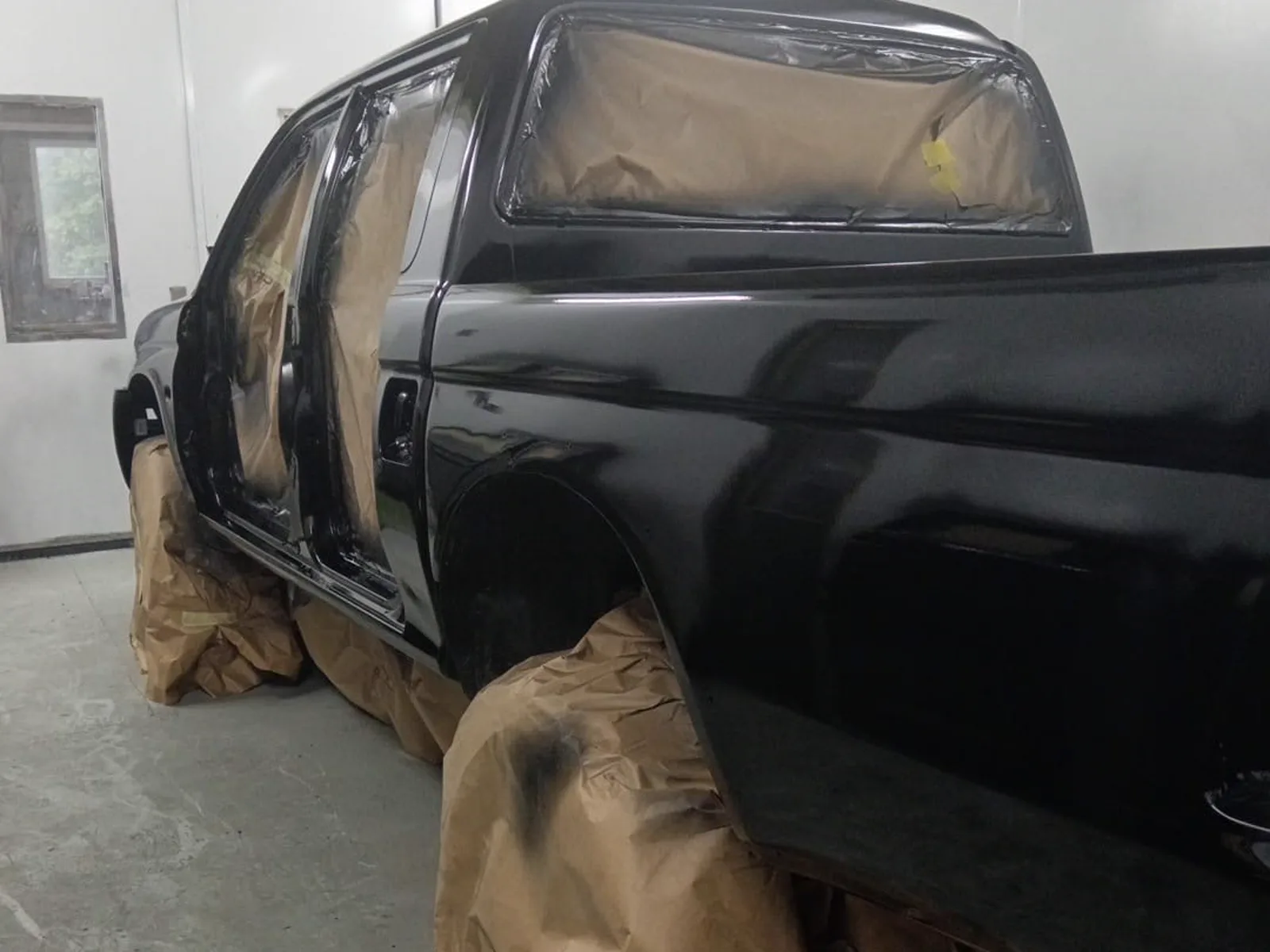 A gloss black Mitsubishi L200 masked up in the paint booth