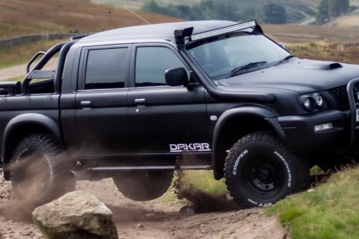 A black STC Dakar Edition L200 kicking up mud on a moorland track