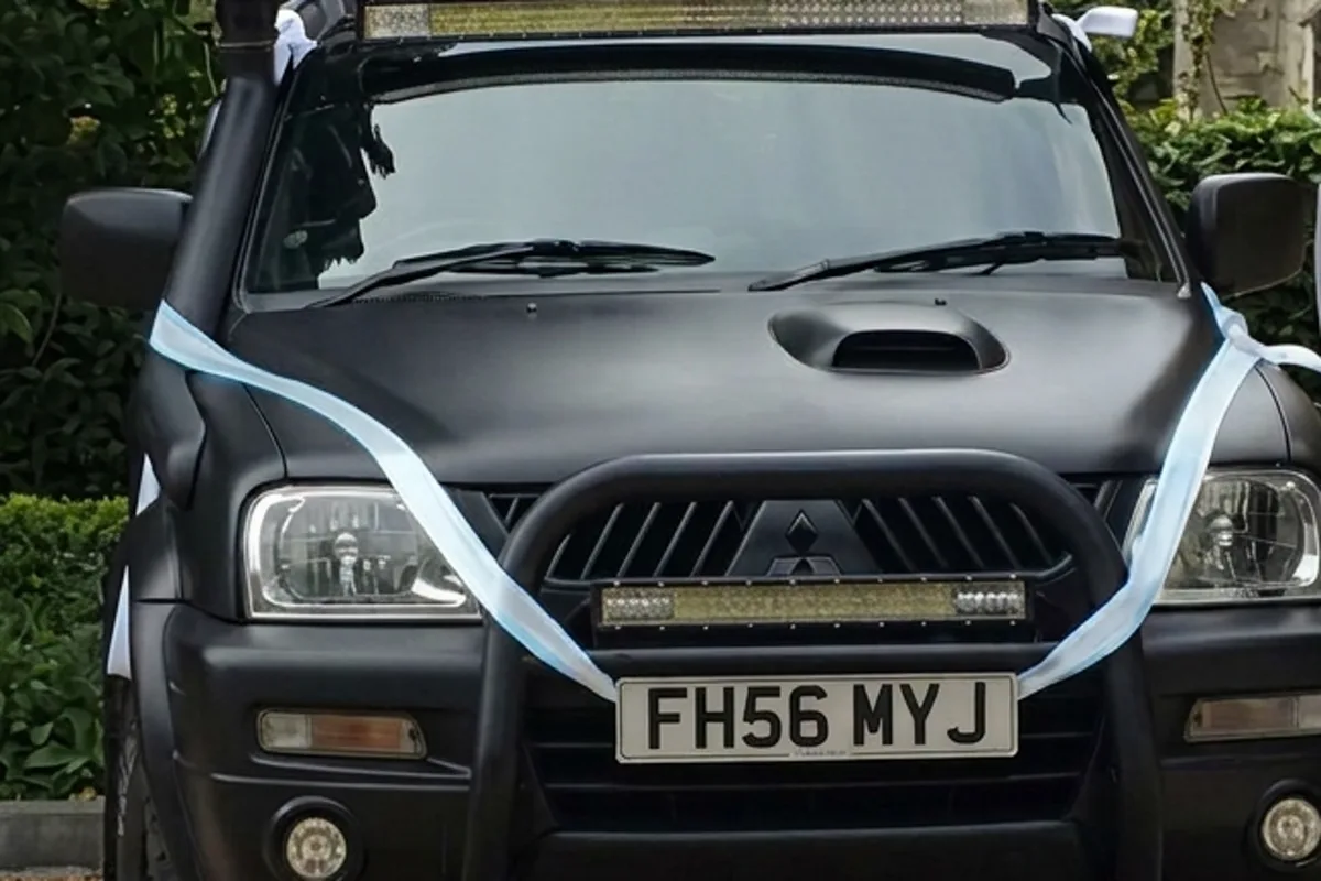 A black STC L200 dressed with white wedding ribbon outside a church