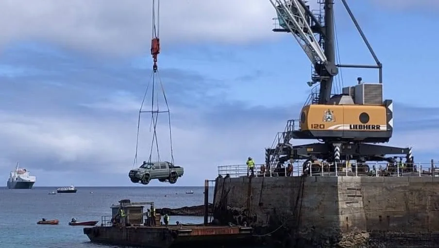 The Dakar lifted by crane at the pier, a ship at anchor behind it